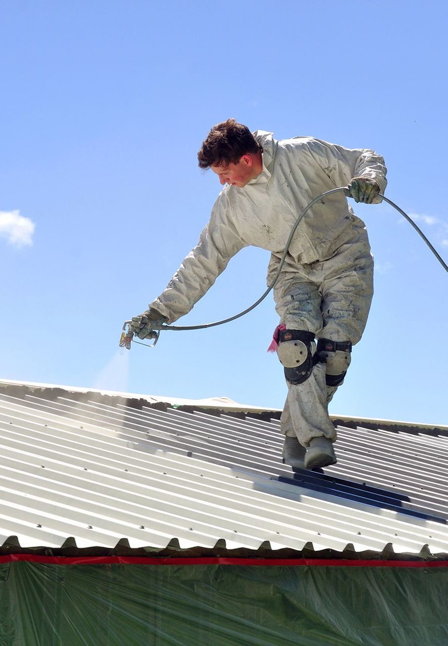 A Man Sprays Paint on the Roof — Roof Restoration Masters In Bonnells Bay, NSW