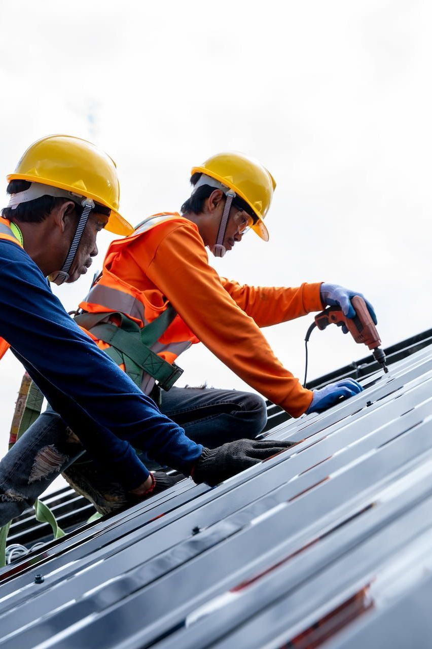 Two Construction Workers Are Working on the Roof — Roof Restoration Masters In Cameron Park, NSW