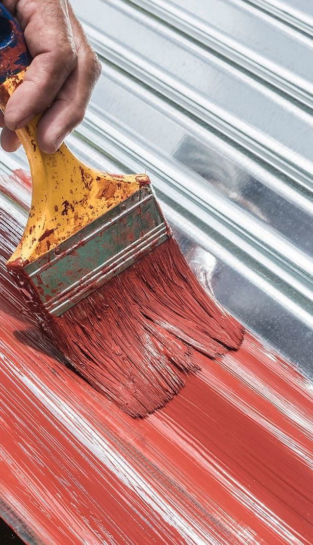 A Person is Painting a Metal Roof With a Brush — Roof Restoration Masters In New Lambton, NSW