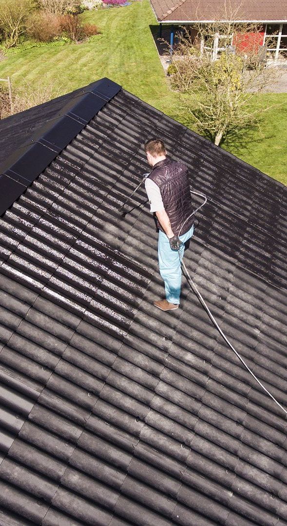 A Man is Spraying a Roof With a Hose — Roof Restoration Masters In Gosford, NSW