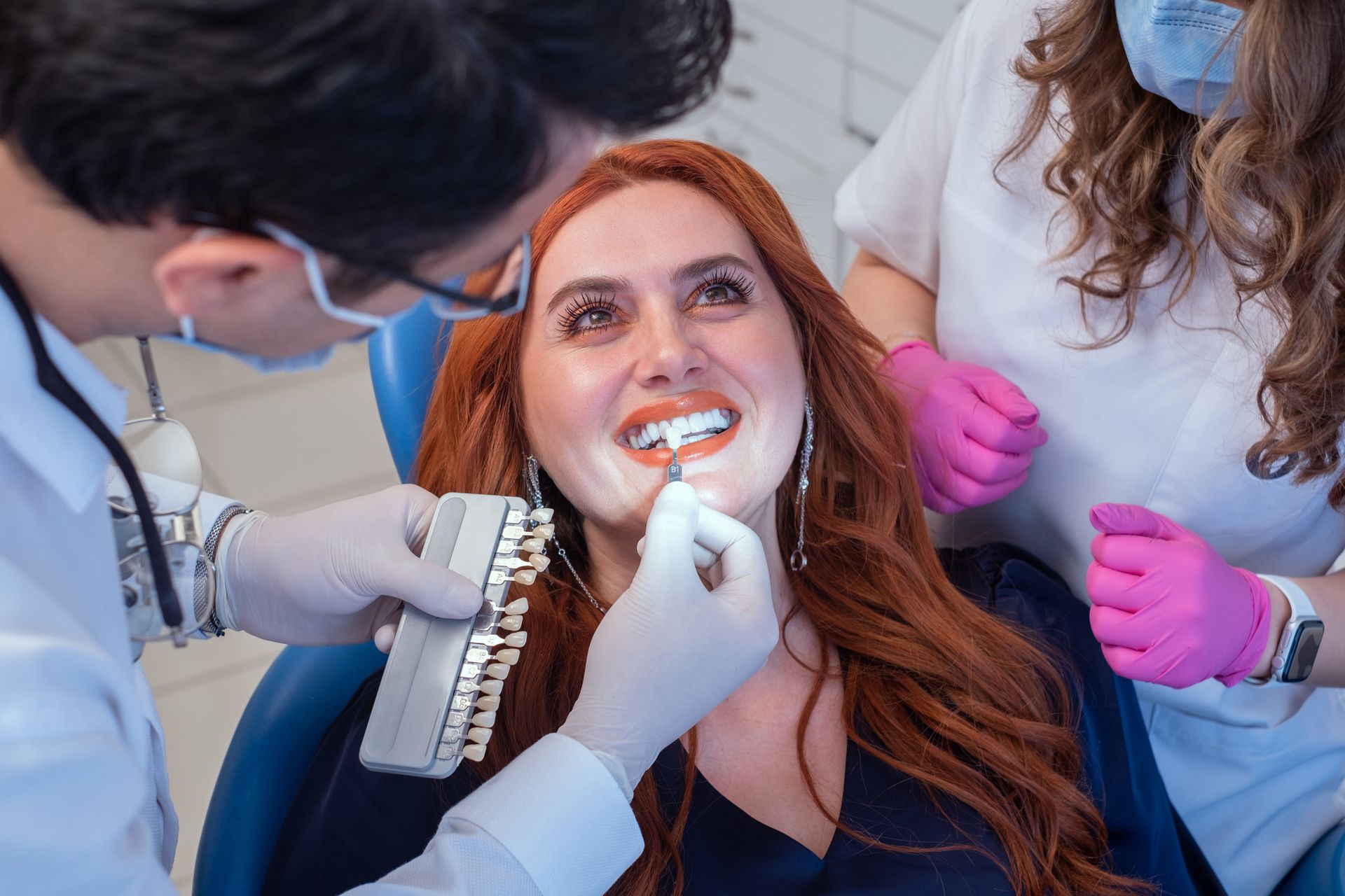 Cosmetic dentists performing teeth shade matching for smile makeover on female patient in clinic.