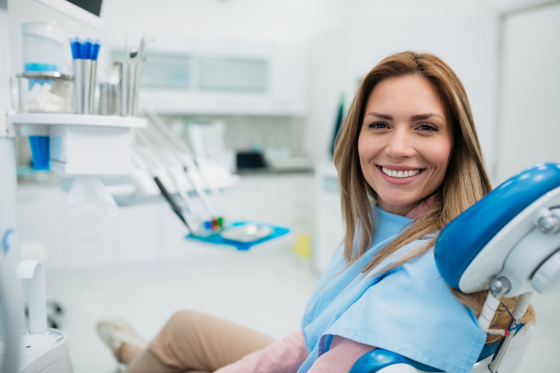 A smiling woman visiting a preventive dentist, sitting on a chair with a blue cloth cover over her