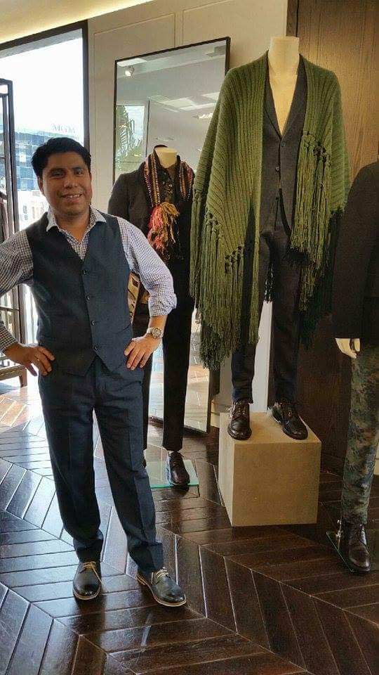 Person in navy suit poses next to mannequins wearing outfits, indoors.