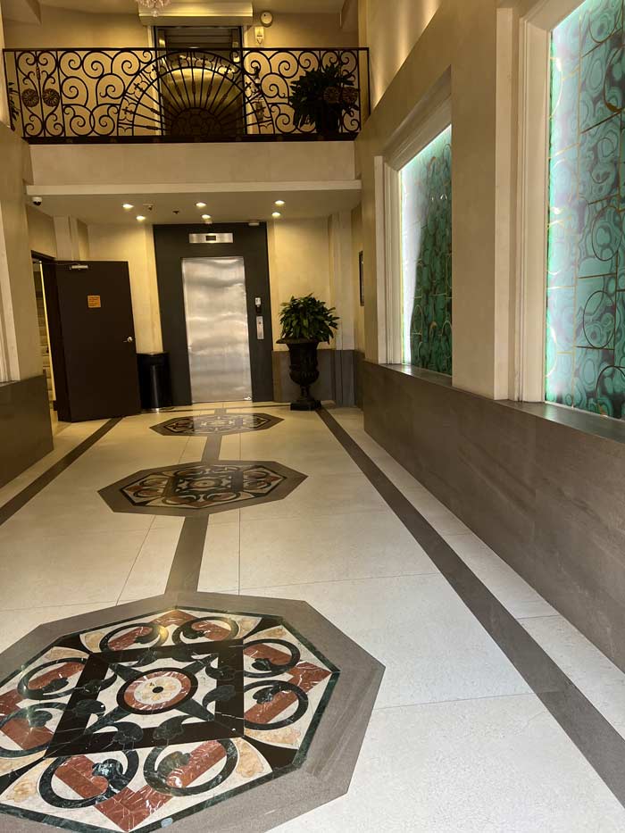 Hallway with ornate floor tiles, elevator, decorative railing, and water feature.