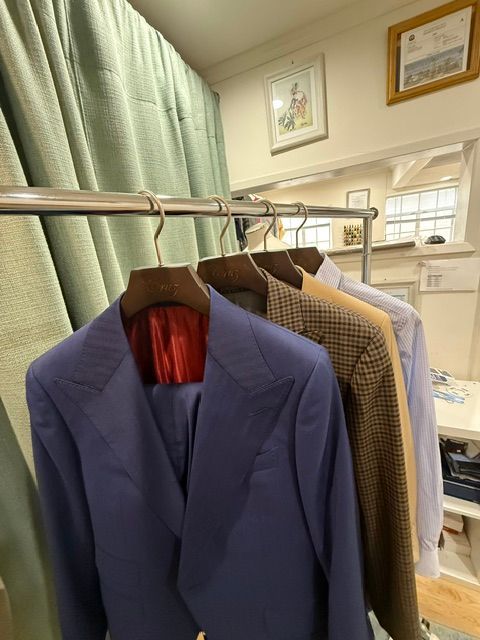 Suits hanging on a metal rack in a tailor shop; blue, brown, and light blue jackets are visible.