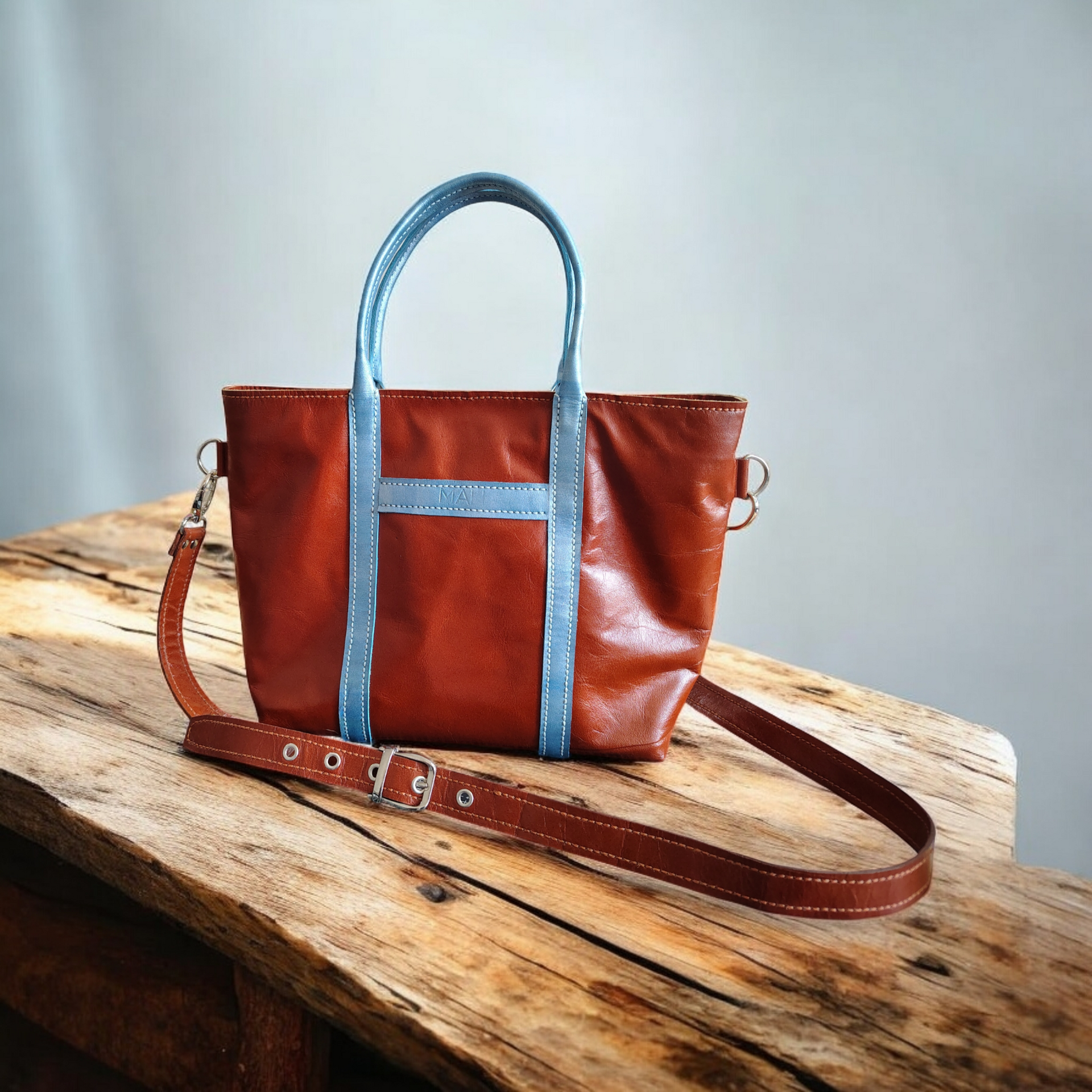 Bolso tote de piel marrón con ribete azul, sobre superficie de madera.