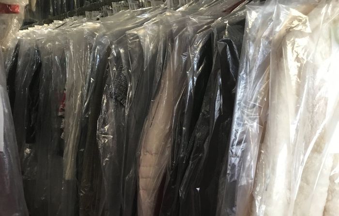 A row of plastic bags filled with clothes hanging on a rack.