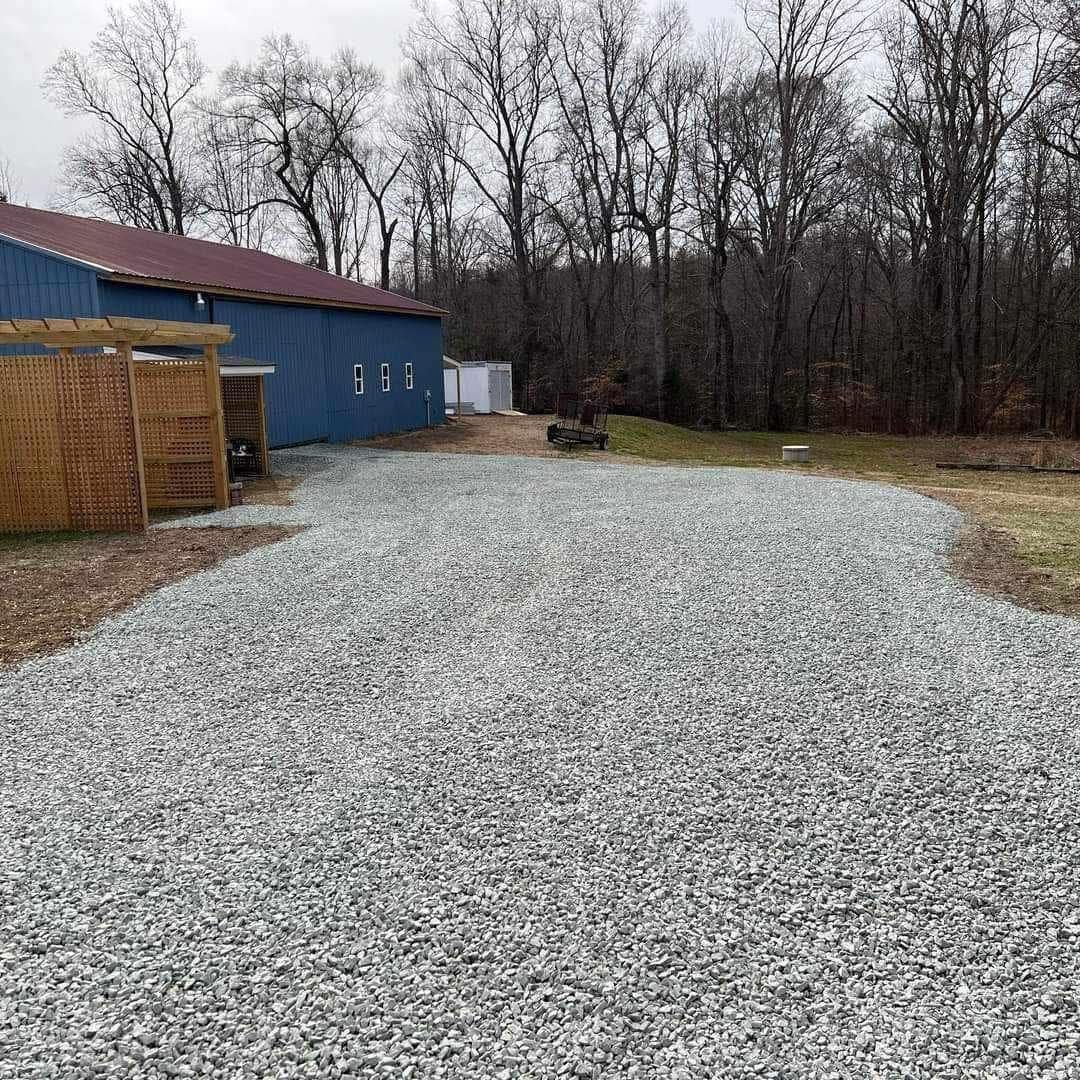 Gravel driveway beside a blue building and leafless trees under an overcast sky