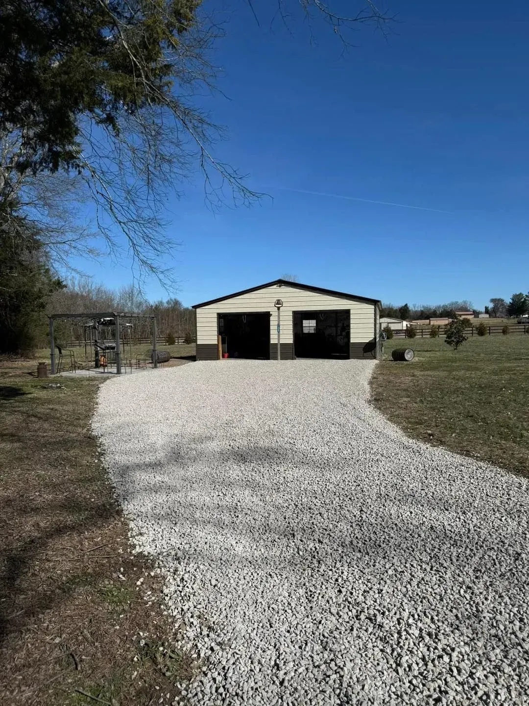 Gravel driveway leading to a beige garage or workshop under a clear blue sky.