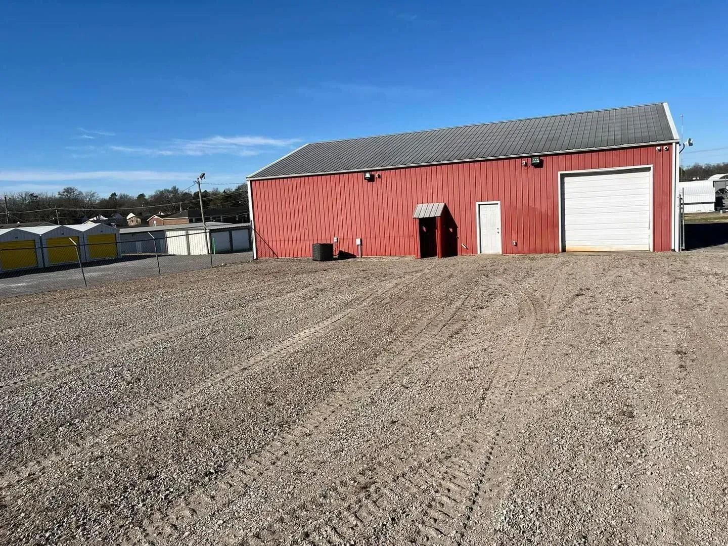 Red barn with white garage door beside a gravel lot under a blue sky