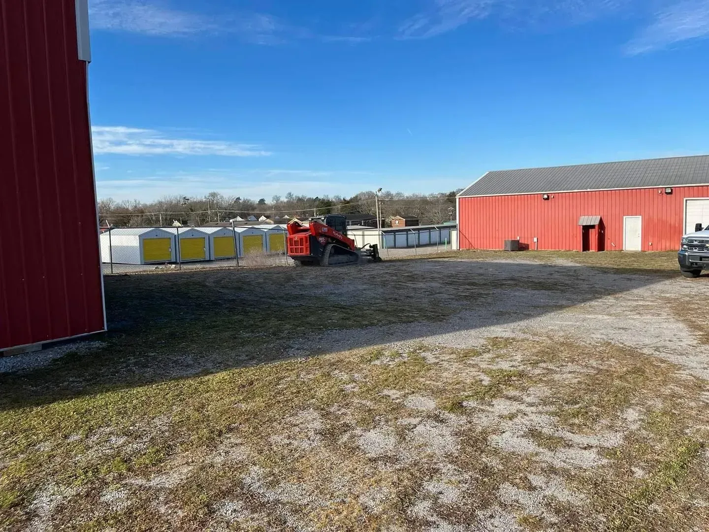 Rural yard with red barns, a red tractor, and a row of bins under a blue sky