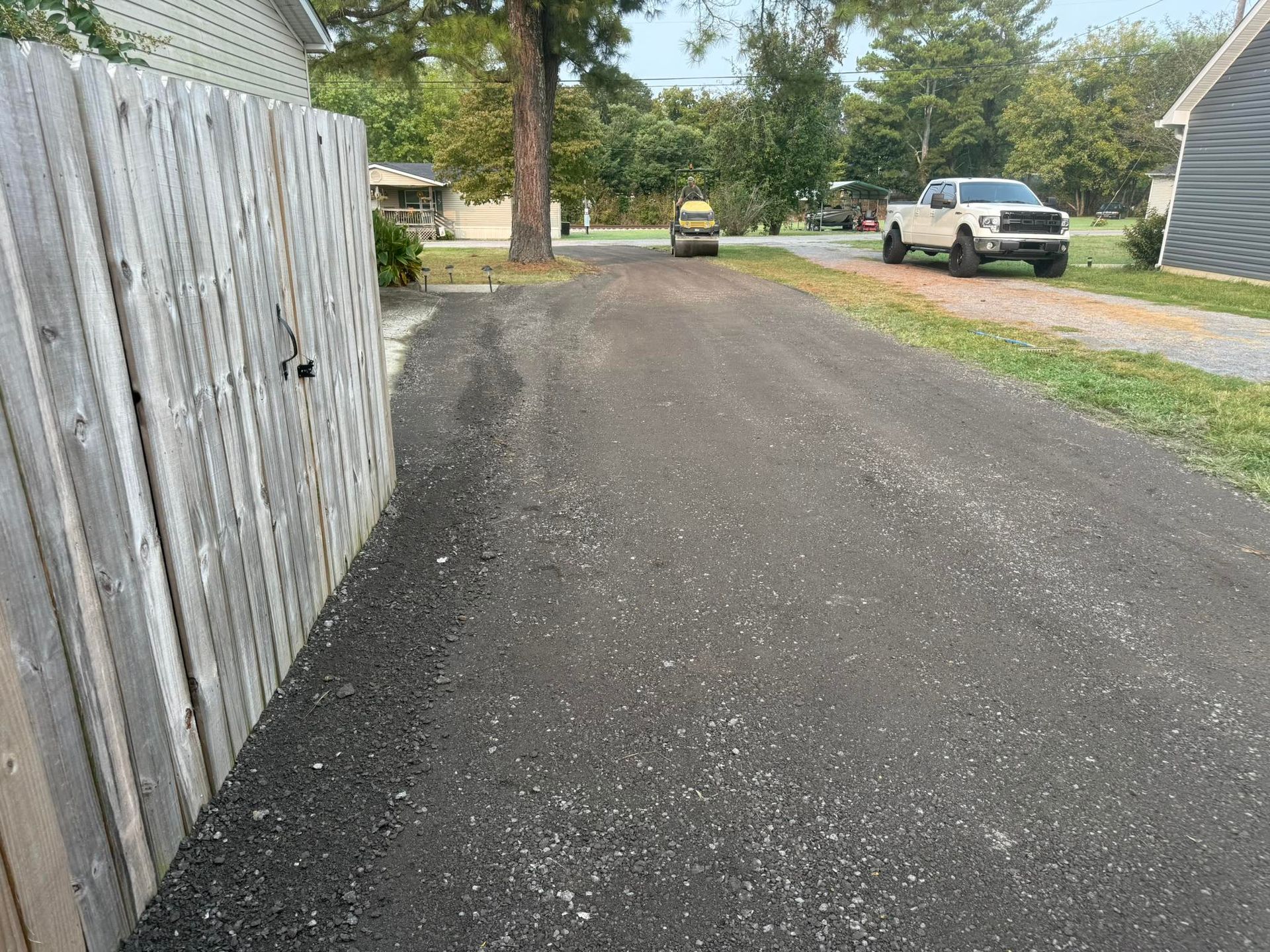 Driveway with a wooden fence on the left, parked vehicles ahead, and trees in a residential area.