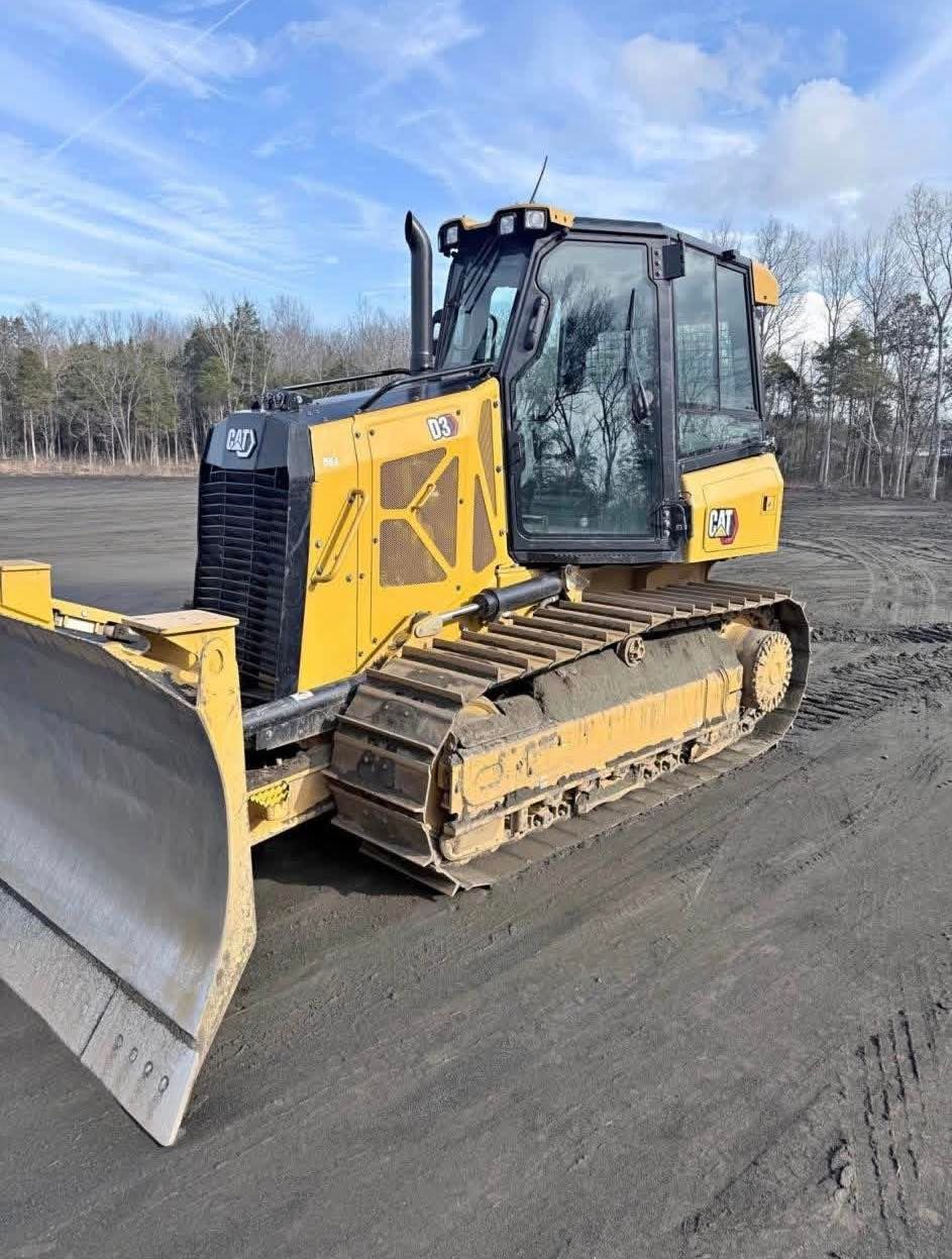 Yellow tracked bulldozer parked on a dirt road under a blue sky