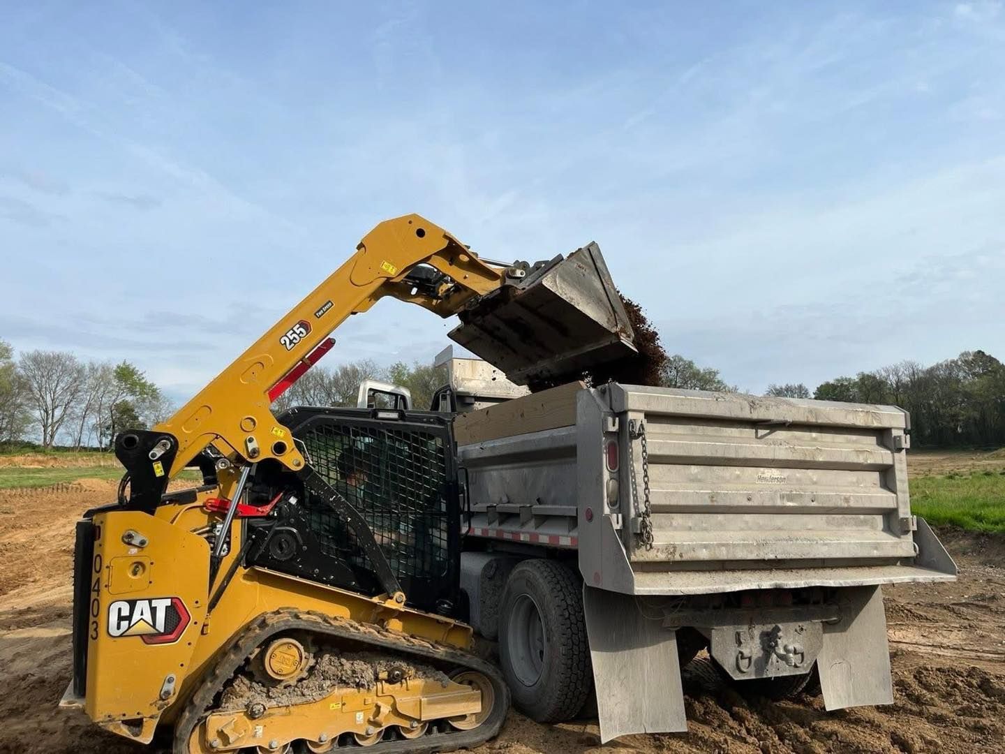 Yellow CAT loader dumping debris into a gray dump truck in a field