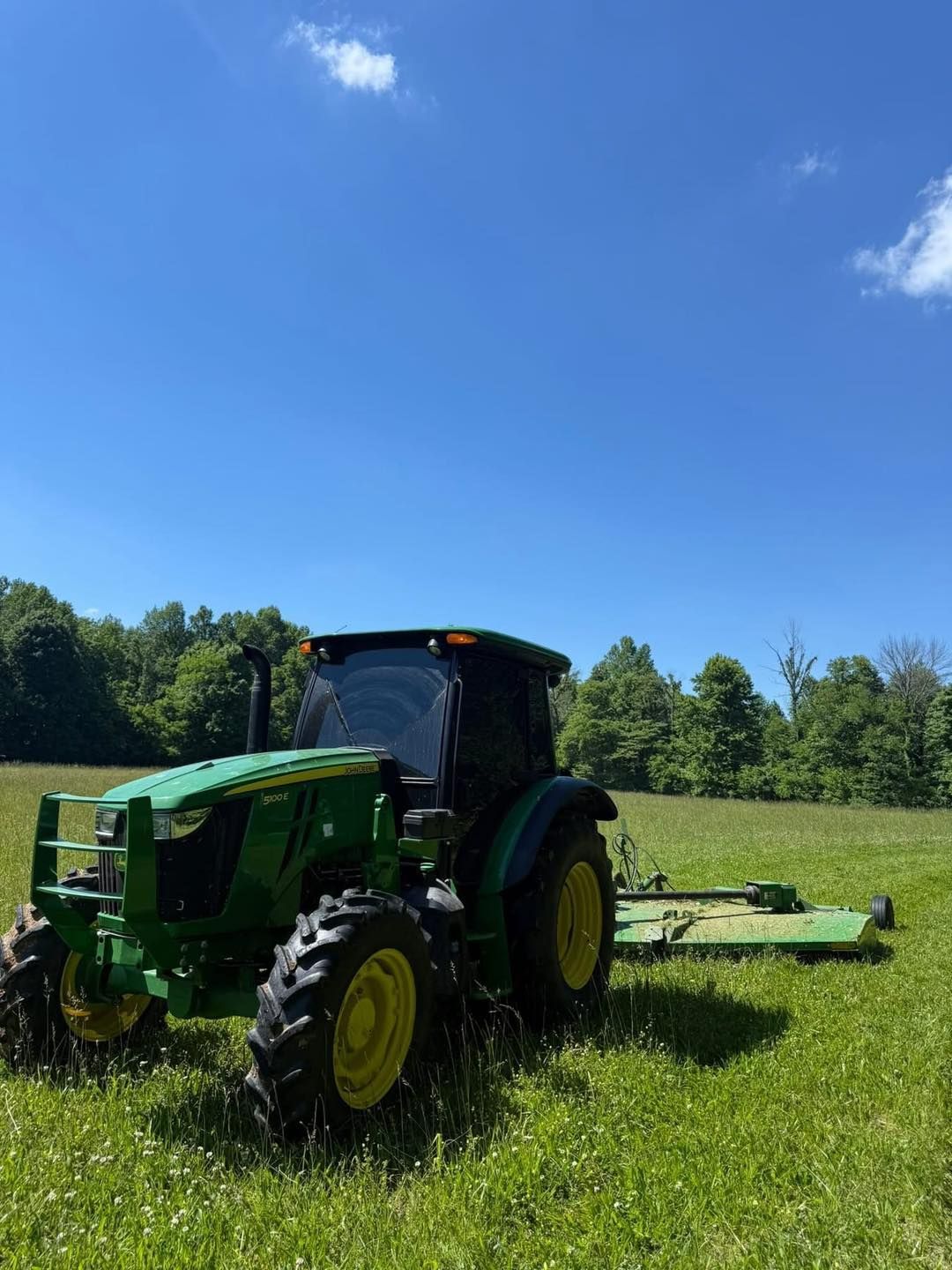 Green tractor mowing a grassy field under a blue sky