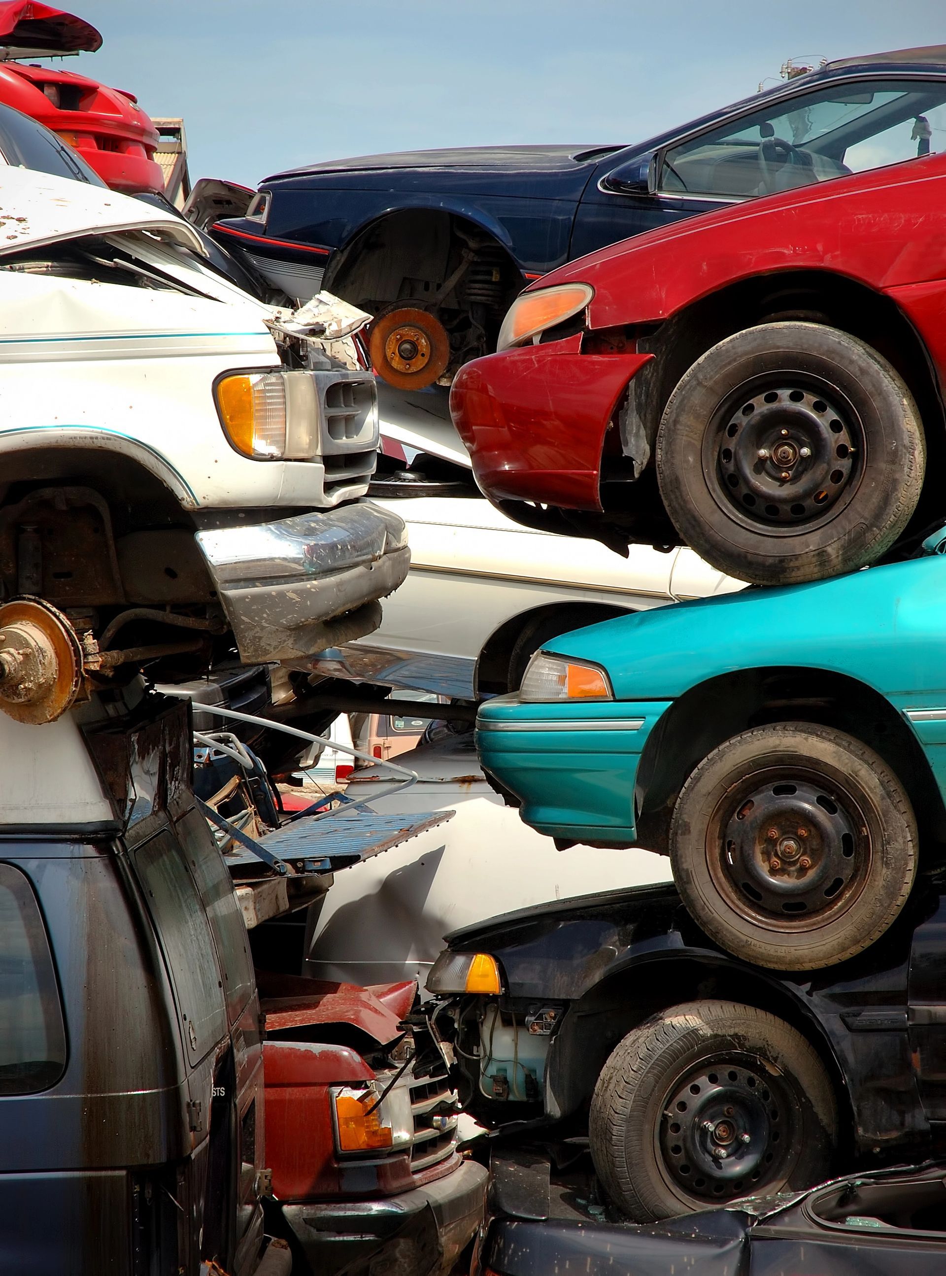 In una discarica, accatastate auto schiacciate, tra cui veicoli rossi, bianchi e turchesi.
