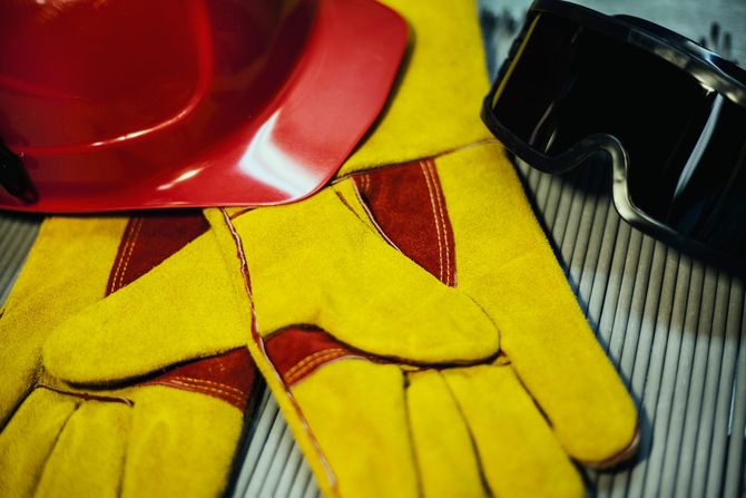 Casco rosso e guanti da lavoro gialli su una superficie grigia