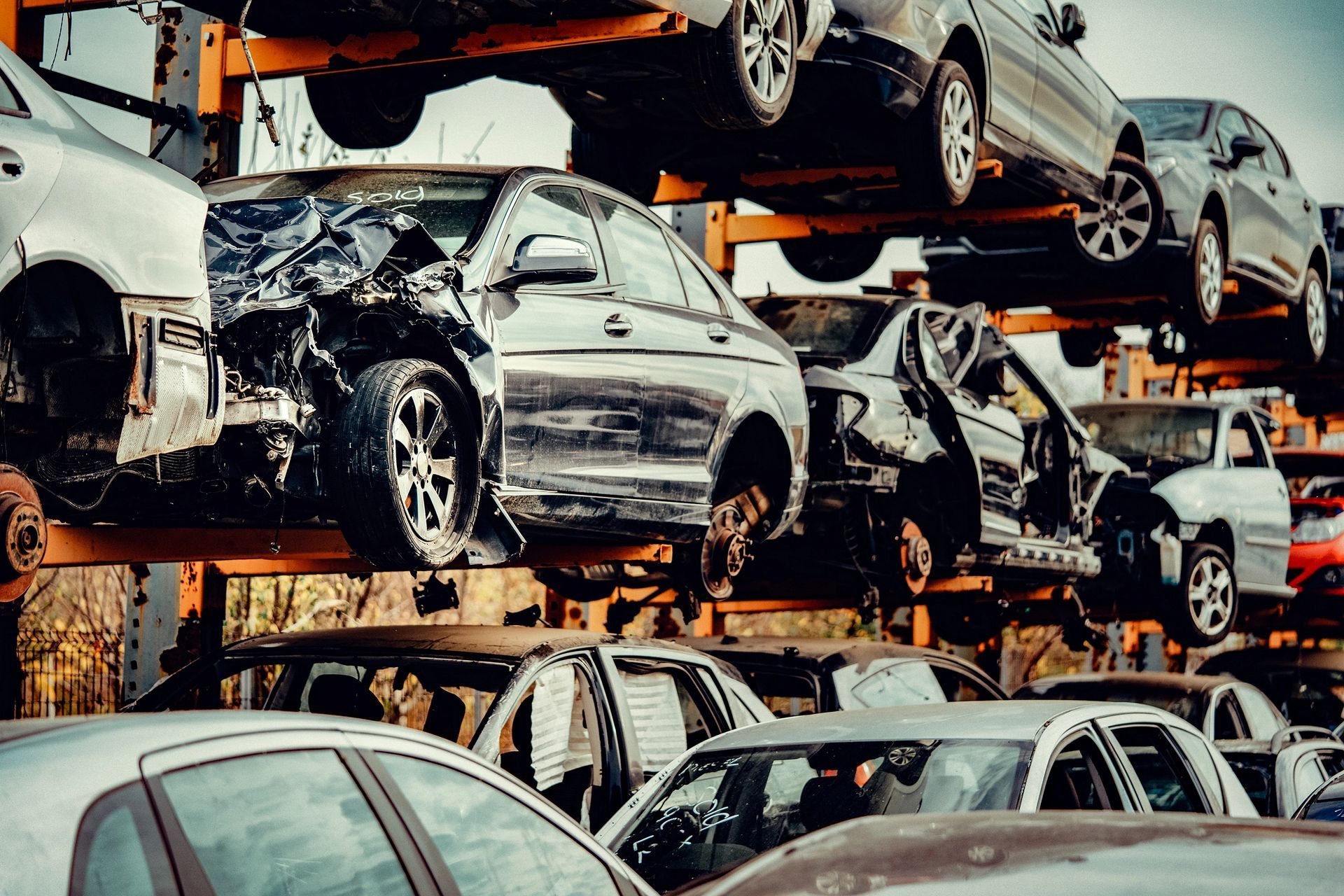 In un deposito di rottami, accatastate auto danneggiate, con veicoli schiacciati ammassati su scaffalature metalliche.