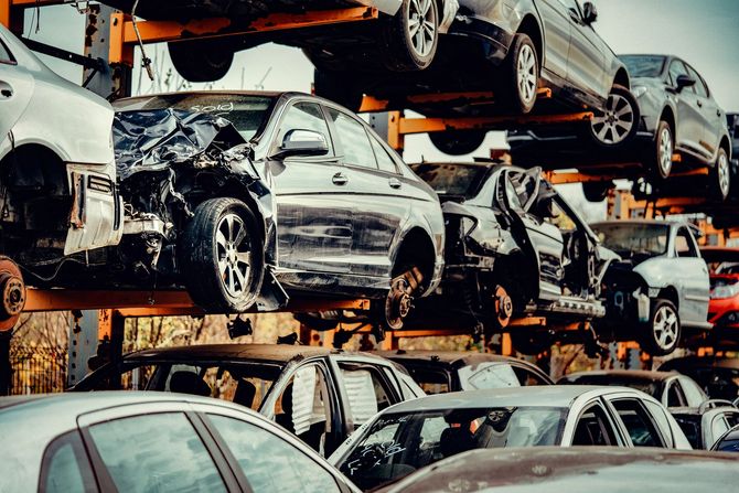In un deposito di rottami, accatastate auto danneggiate, con veicoli schiacciati ammassati su scaffalature metalliche.