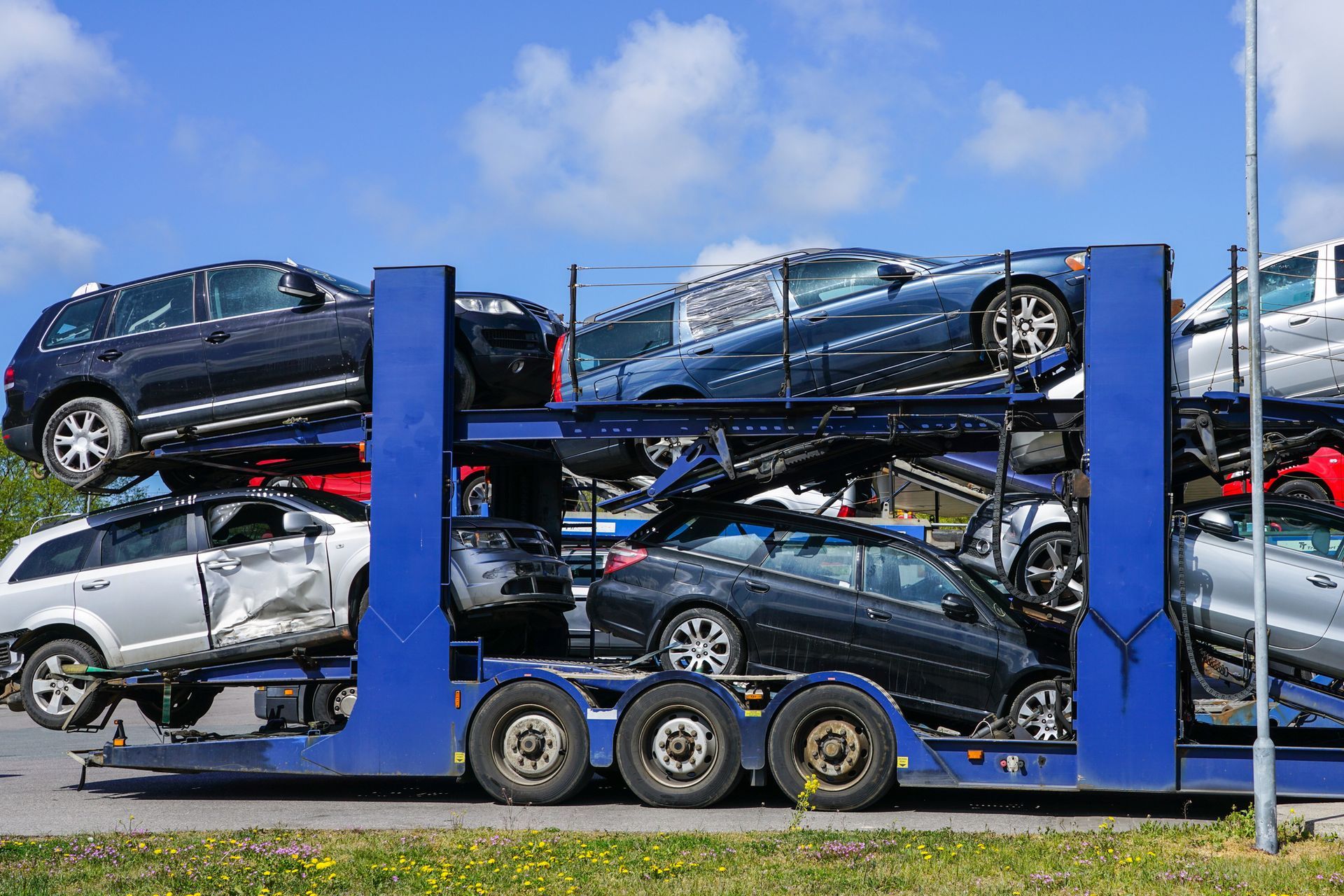 Un rimorchio portauto carico con diversi veicoli impilati su due livelli, sotto un cielo azzurro.