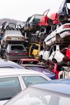 In una discarica, accatastate e schiacciate automobili, con veicoli rossi, bianchi e argento ammassati uno sull'altro.