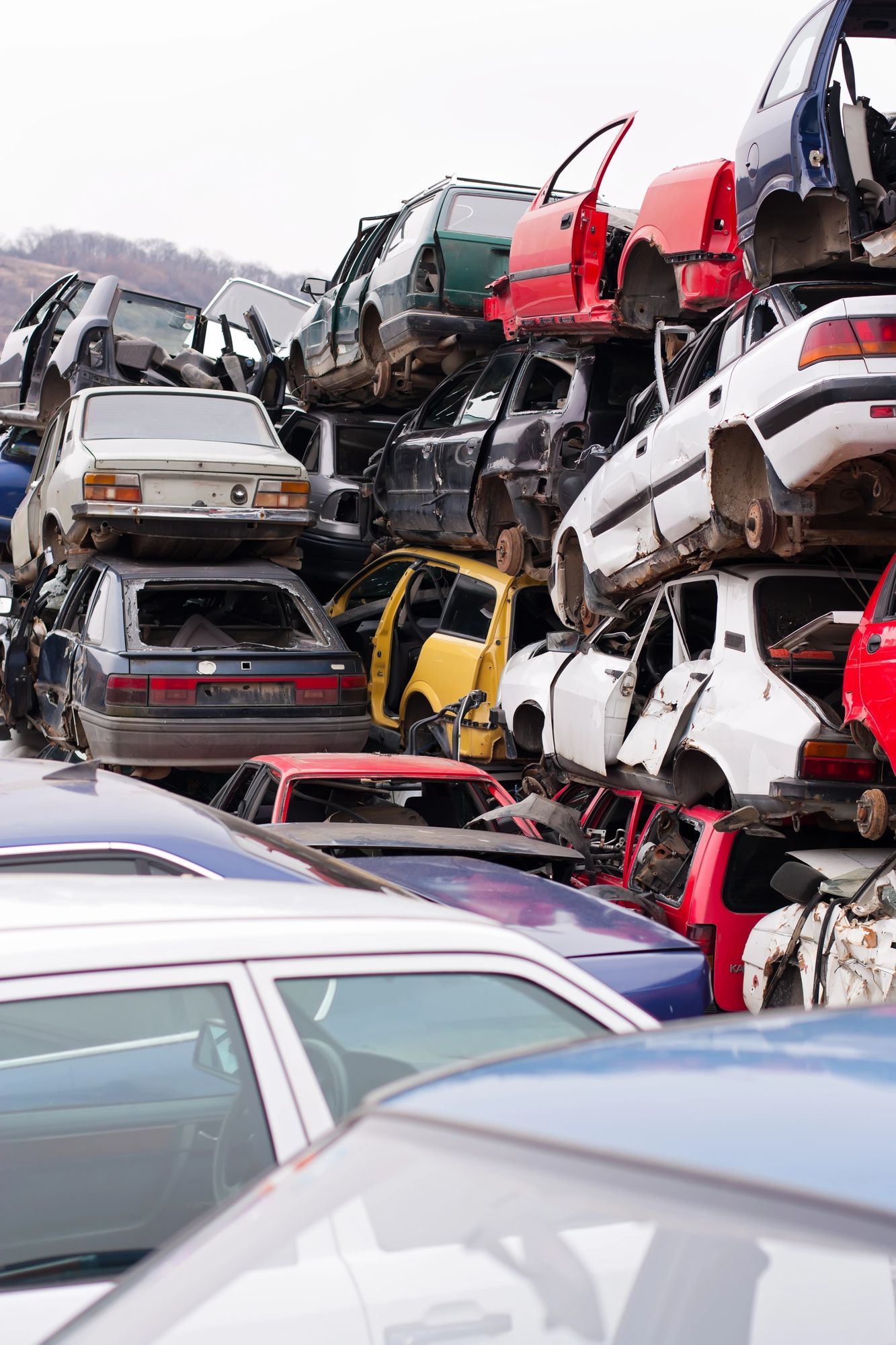 In una discarica, accatastate e schiacciate automobili, con veicoli rossi, bianchi e argento ammassati uno sull'altro.