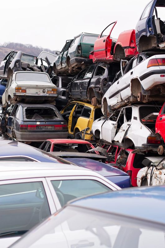 In una discarica, accatastate e schiacciate automobili, con veicoli rossi, bianchi e argento ammassati uno sull'altro.