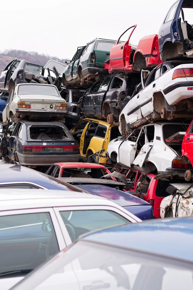 In una discarica, accatastate e schiacciate automobili, con veicoli rossi, bianchi e argento ammassati uno sull'altro.
