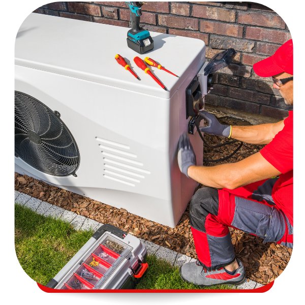 Technician in red outfit working on a white heat pump, tools nearby.