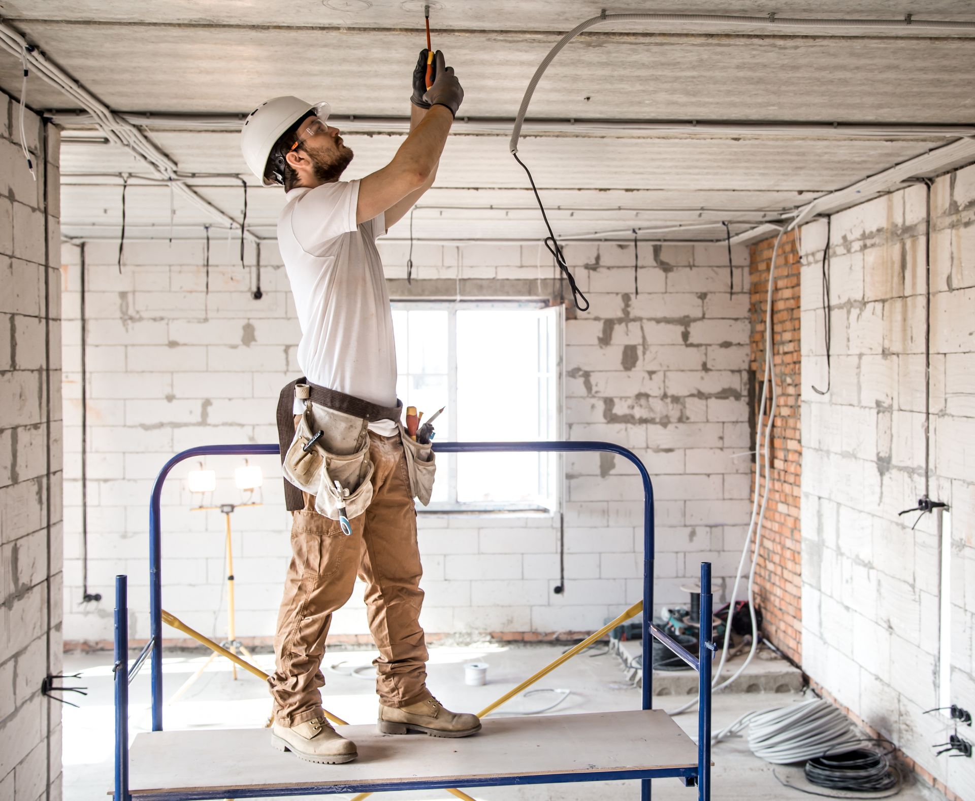 Construction worker installs wiring on scaffolding in unfinished building.