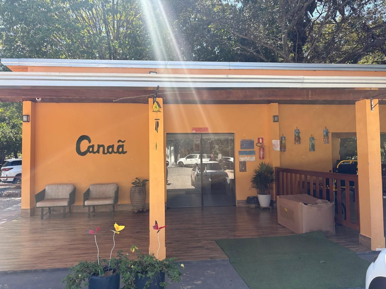 Fachada laranja de um café com pátio coberto, bancos e entrada de vidro iluminada pela luz do dia.
