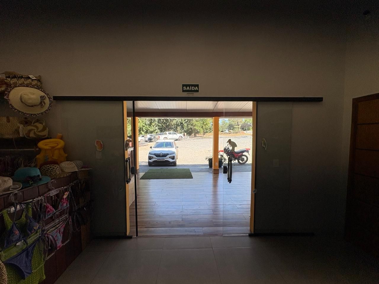 Vista do interior através de portas duplas abertas para uma entrada de automóveis iluminada, com um carro estacionado e uma pessoa do lado de fora.