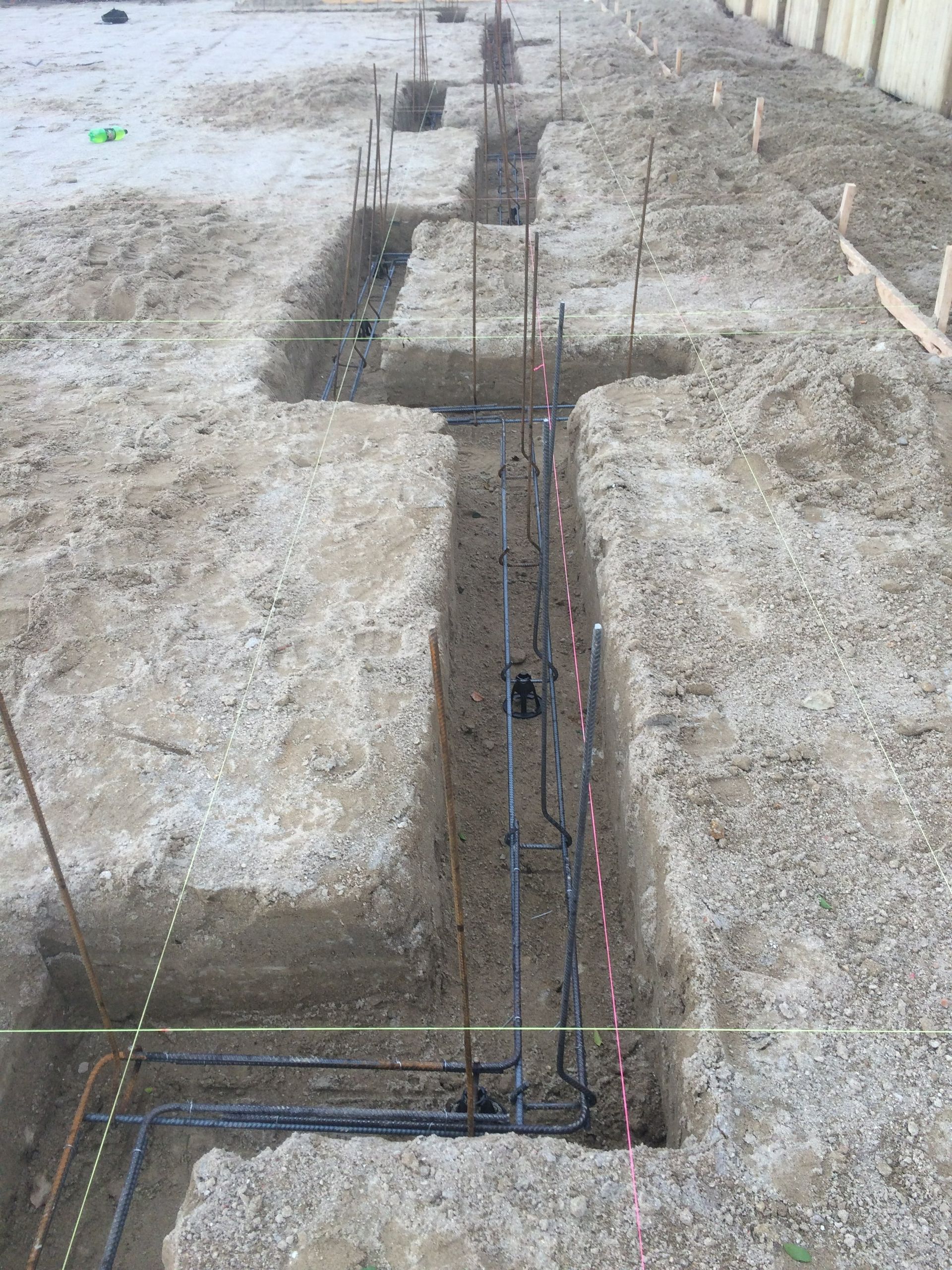 Trenches dug for foundation, with plumbing and rebar visible. Construction site outdoors.