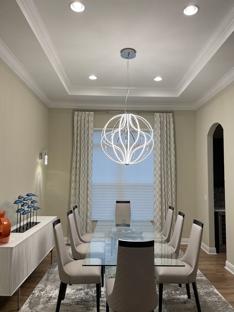 A dining room with a glass table, six chairs, a sideboard with blue decor, and a large, modern spherical chandelier.