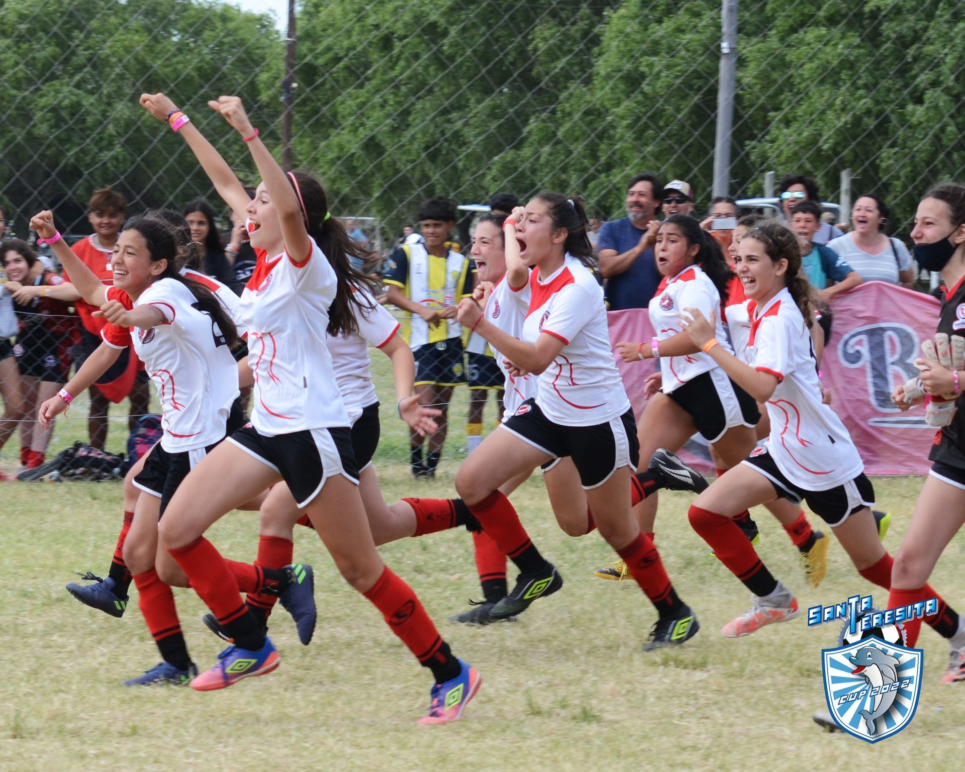 Equipo de fútbol con uniformes blancos y rojos celebrando una victoria en un campo verde.