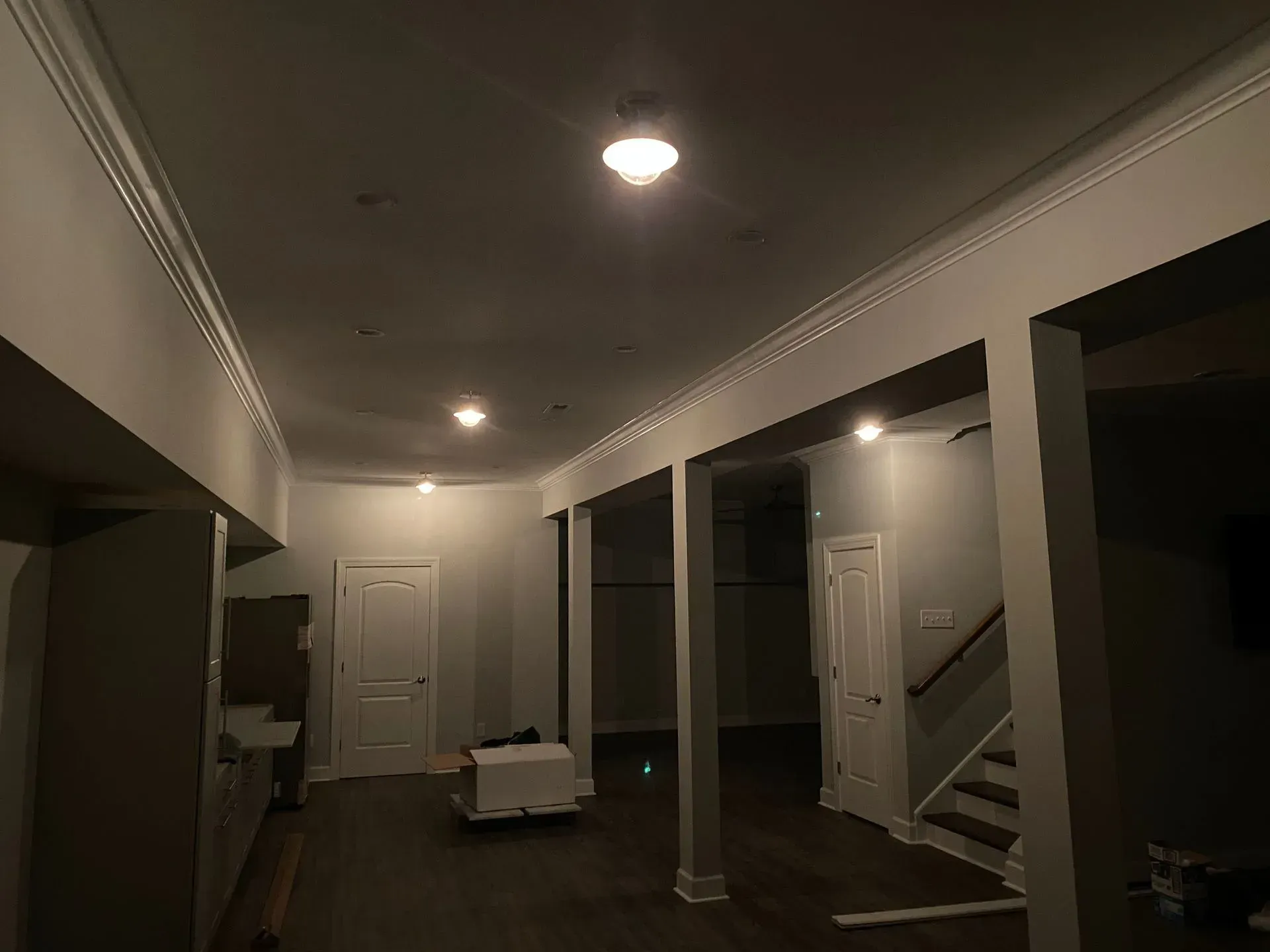 A dim, finished basement with white trim, gray walls, and several recessed lights.
