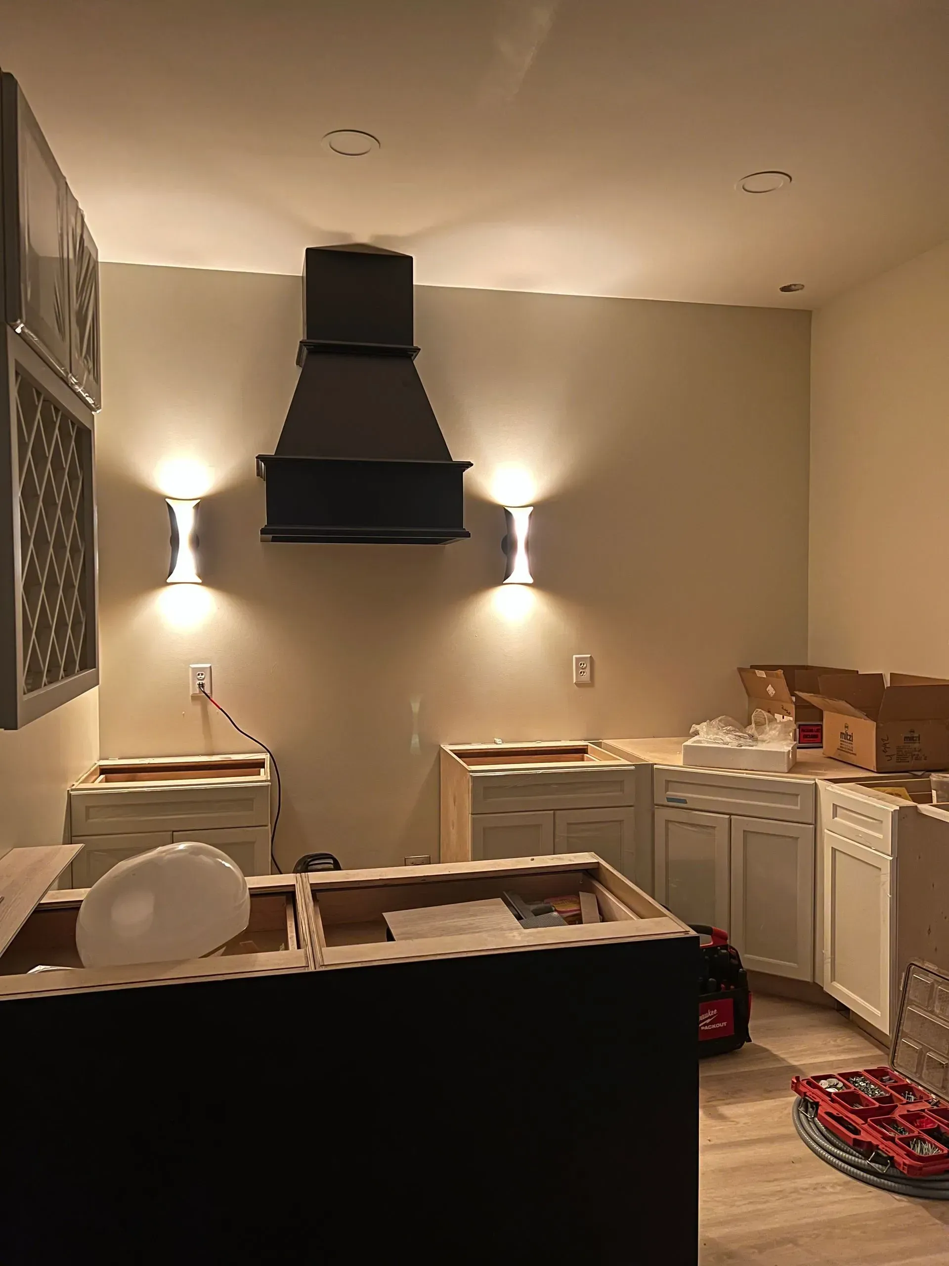 Kitchen under construction with cabinets, range hood, and sconce lighting.