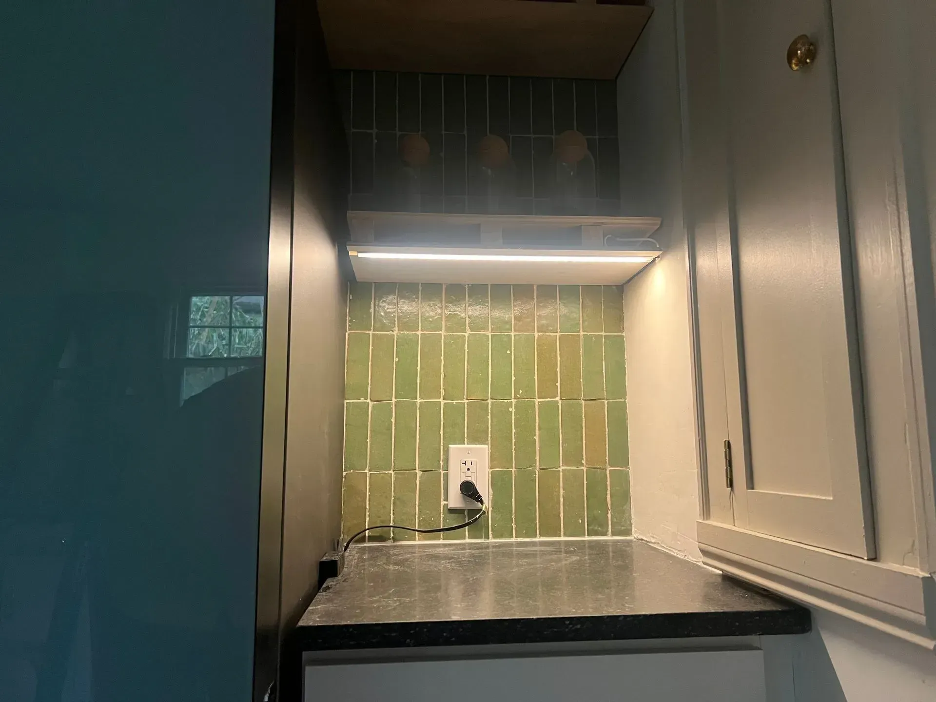 Green tiled backsplash in a kitchen niche, with countertop and under-cabinet LED lighting.
