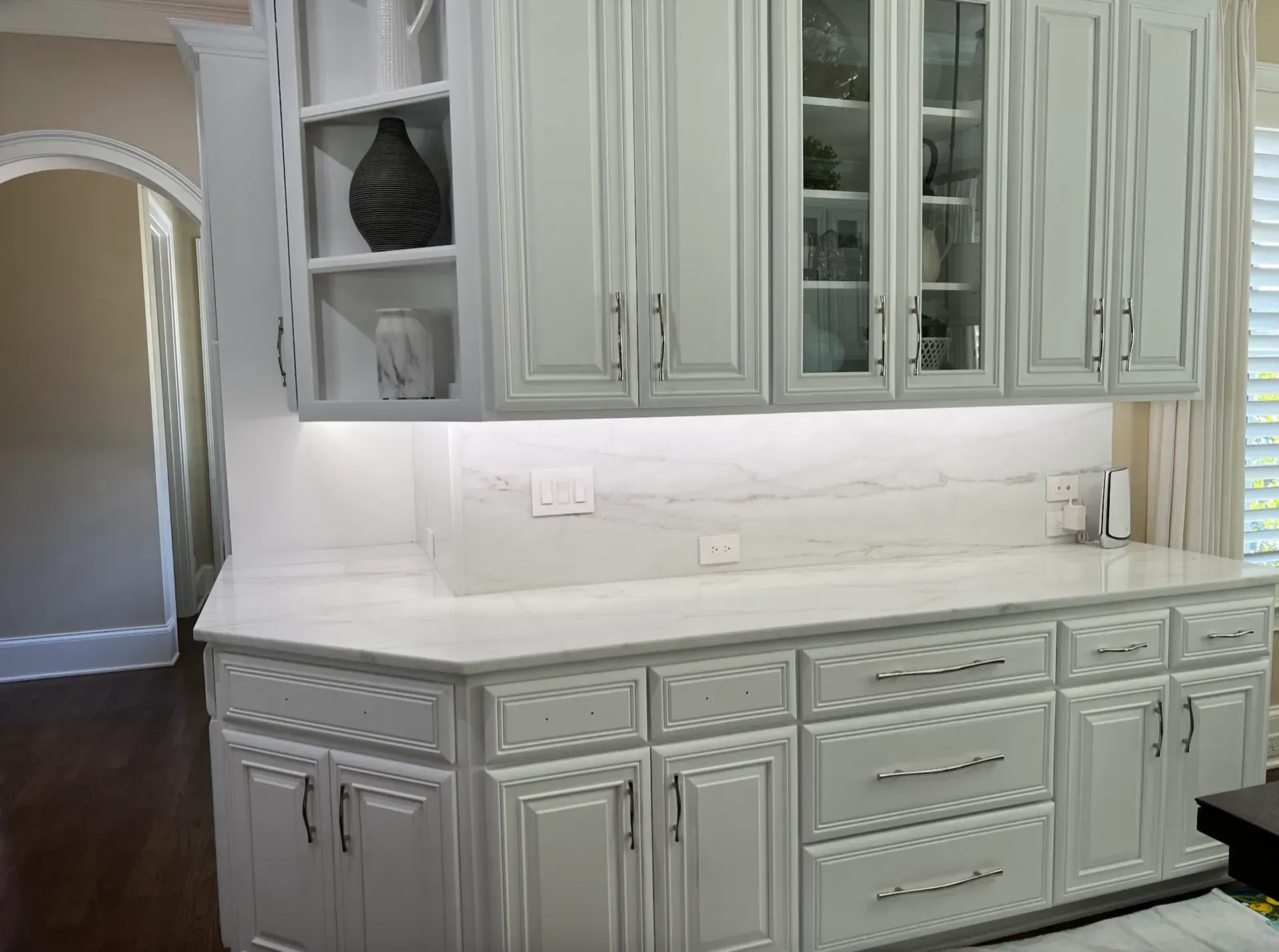 White kitchen cabinets with glass doors, countertop, and built-in lighting.