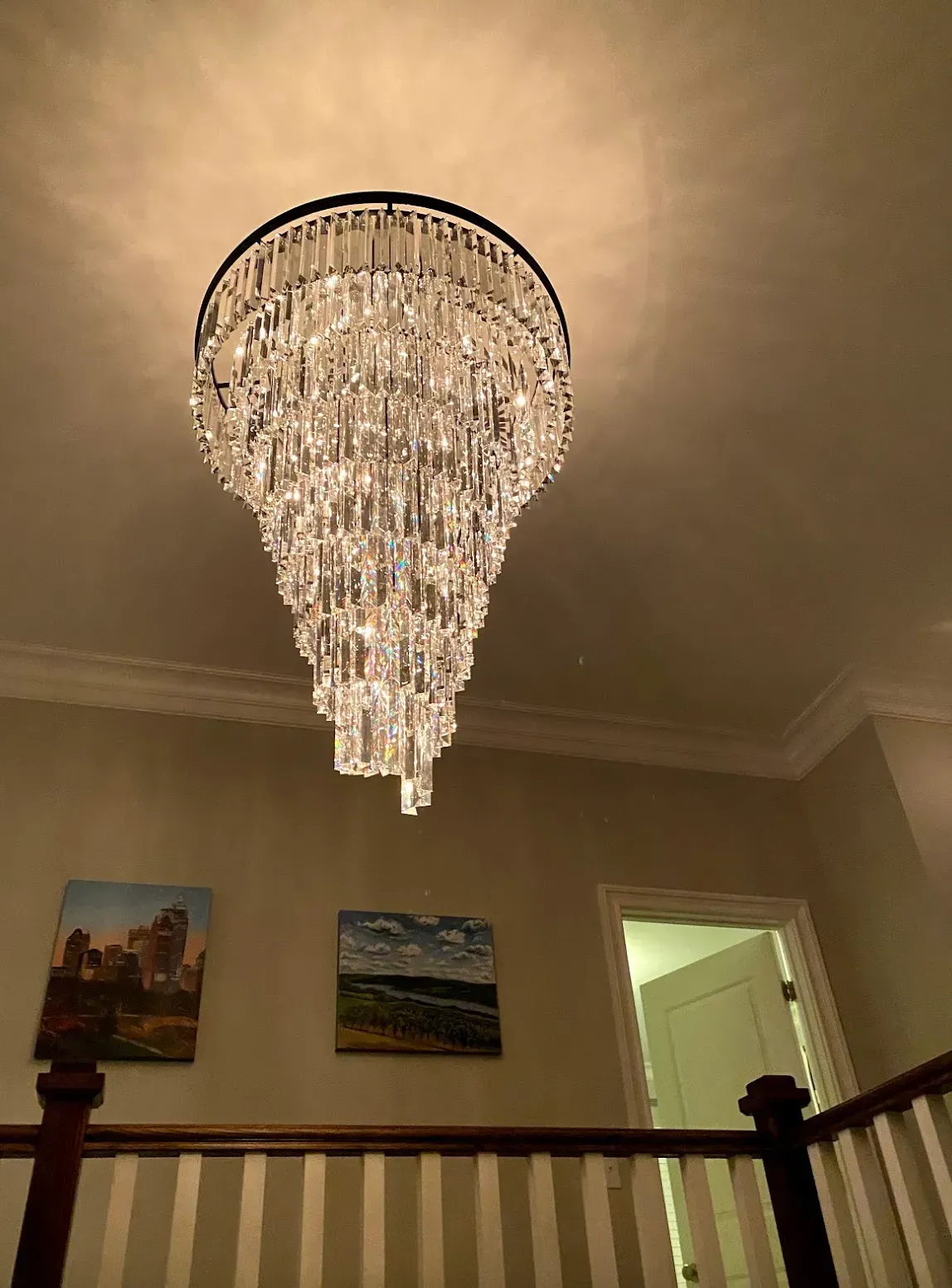 Crystal chandelier hanging above a staircase, illuminating the hallway. Artwork on the wall.