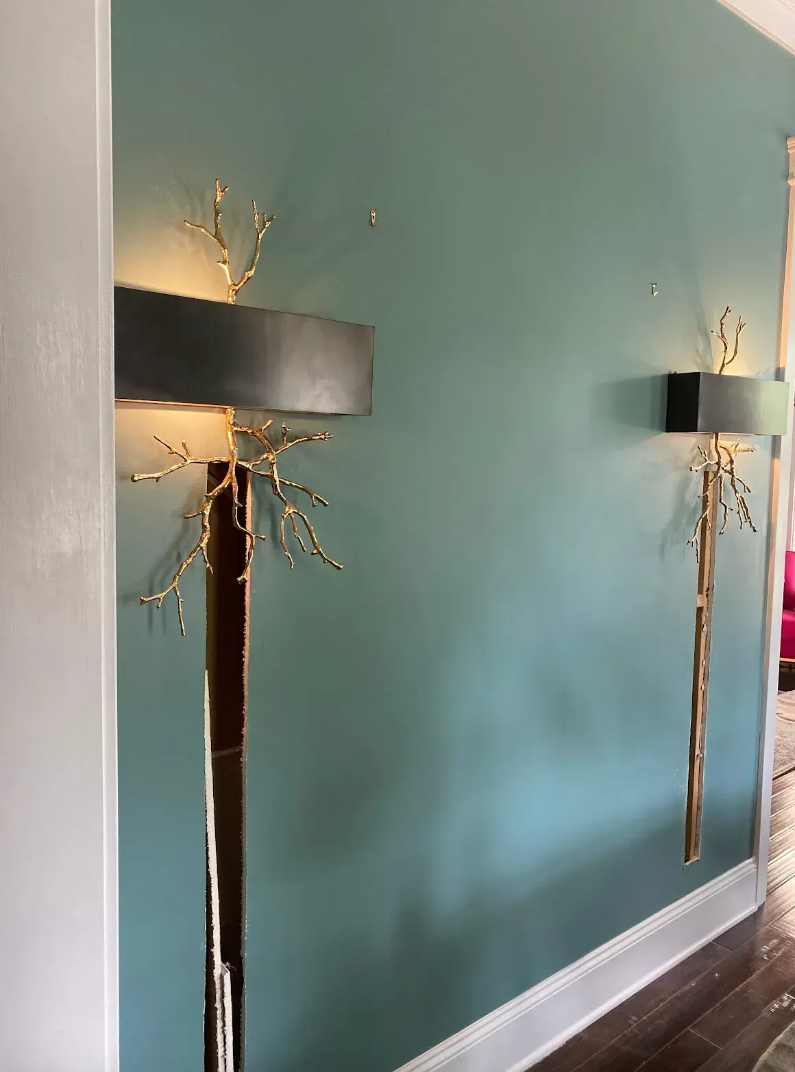 Two gold branch wall sconces on teal wall, near doorframe.