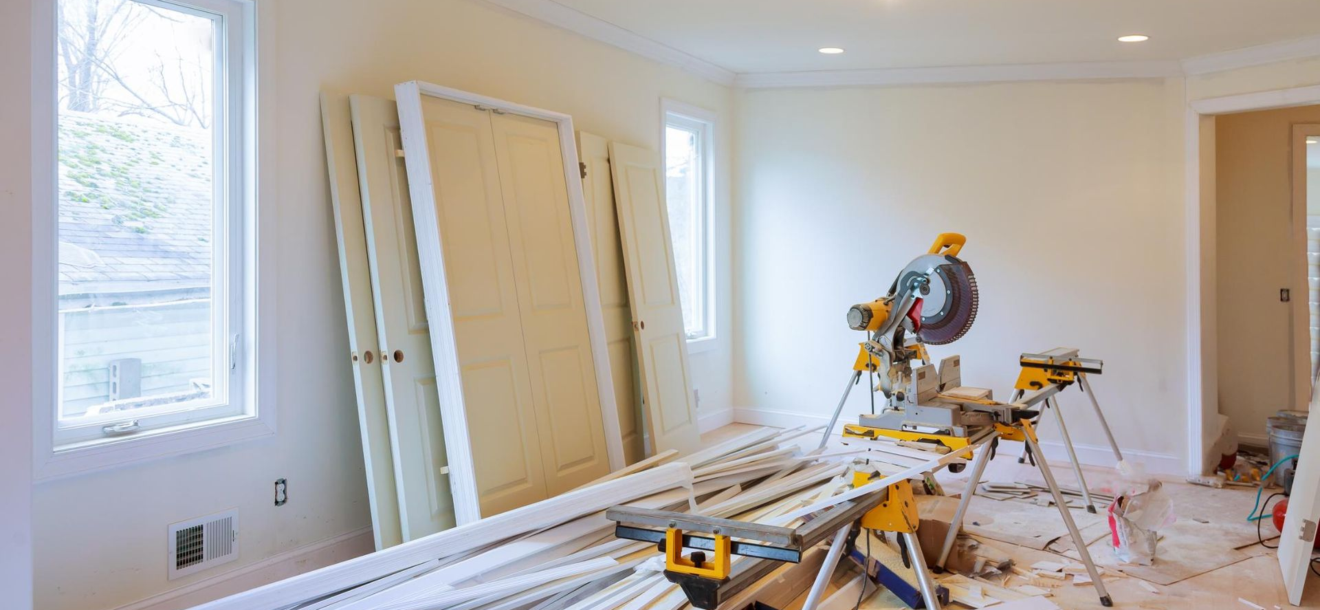Interior room under renovation with a miter saw, trim, doors, and debris.