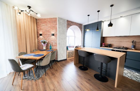 Modern kitchen with dining area, featuring a brick wall, island with stools, and wooden floors.