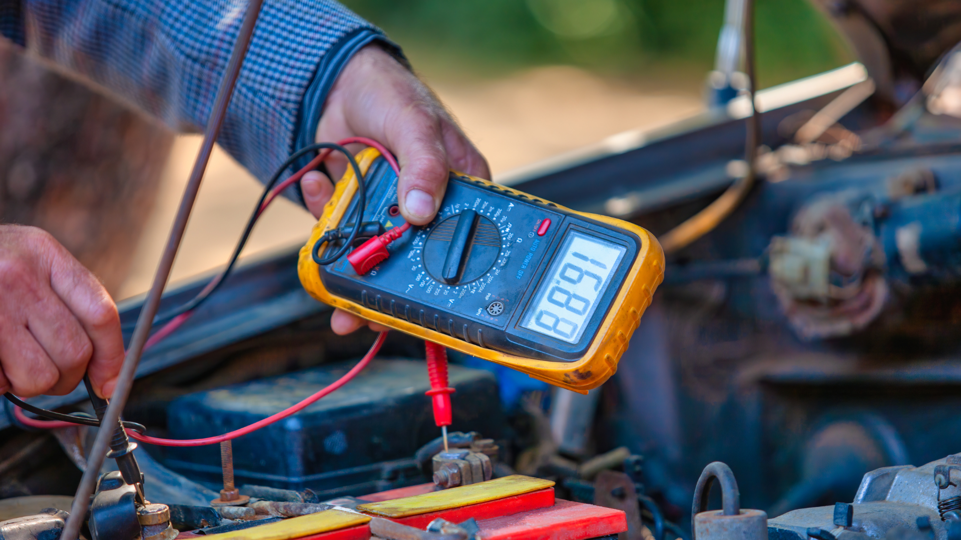 A person is using a multimeter to test a car battery.