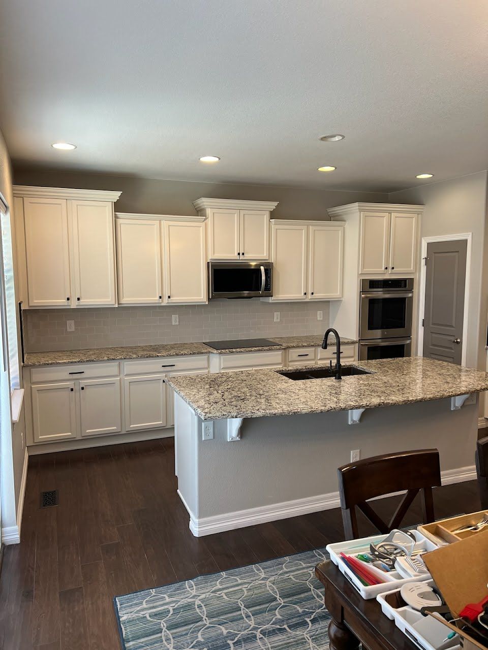 White kitchen with island, granite countertops, and dark wood floors.
