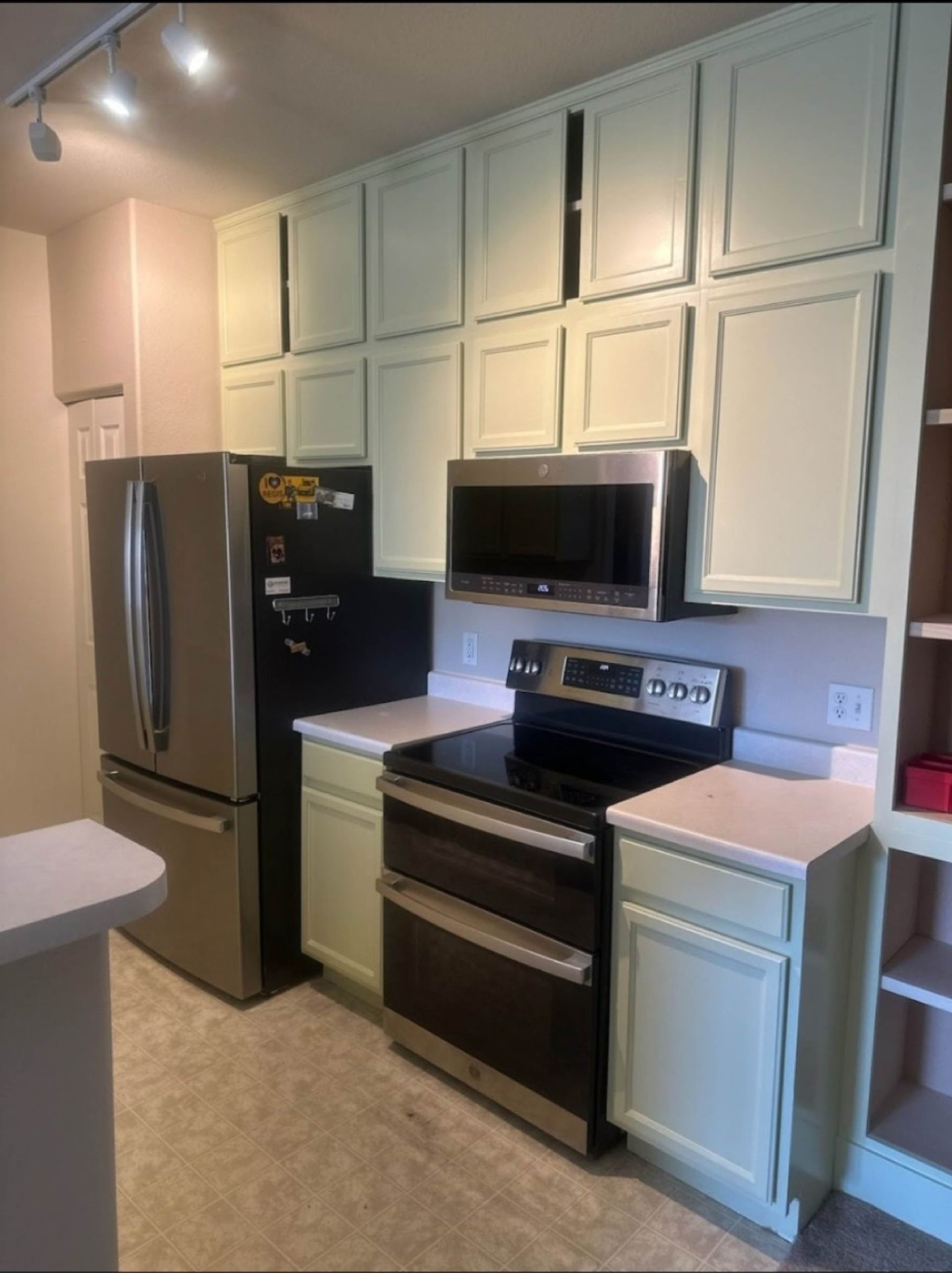 Kitchen with light green cabinets, stainless steel appliances, and a stovetop.