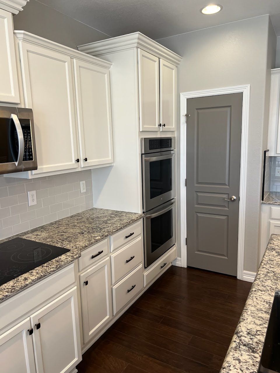 White kitchen cabinets with granite countertops, stainless steel appliances, and a gray pantry door.