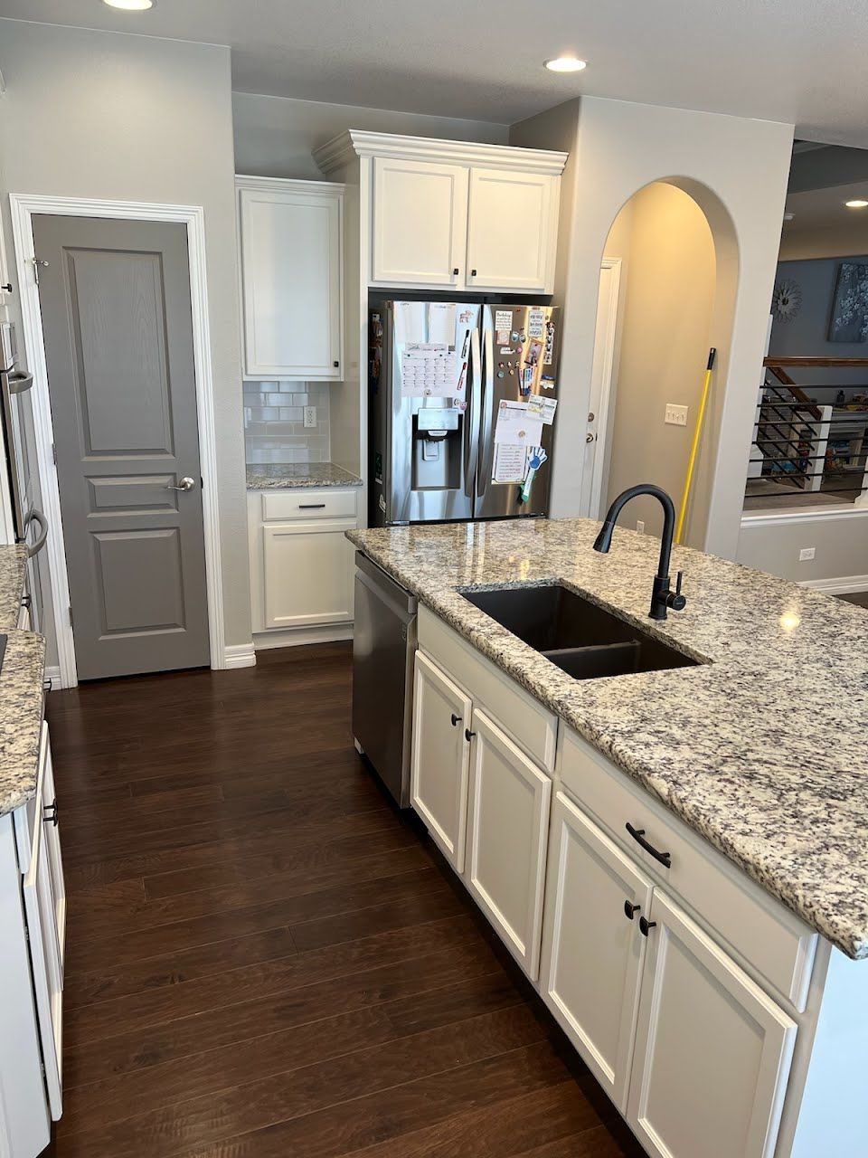 Kitchen with white cabinets, granite countertop, stainless steel appliances, dark wood floor.