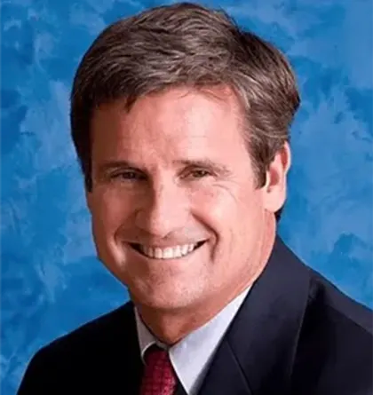 Man in suit smiles against a blue background.