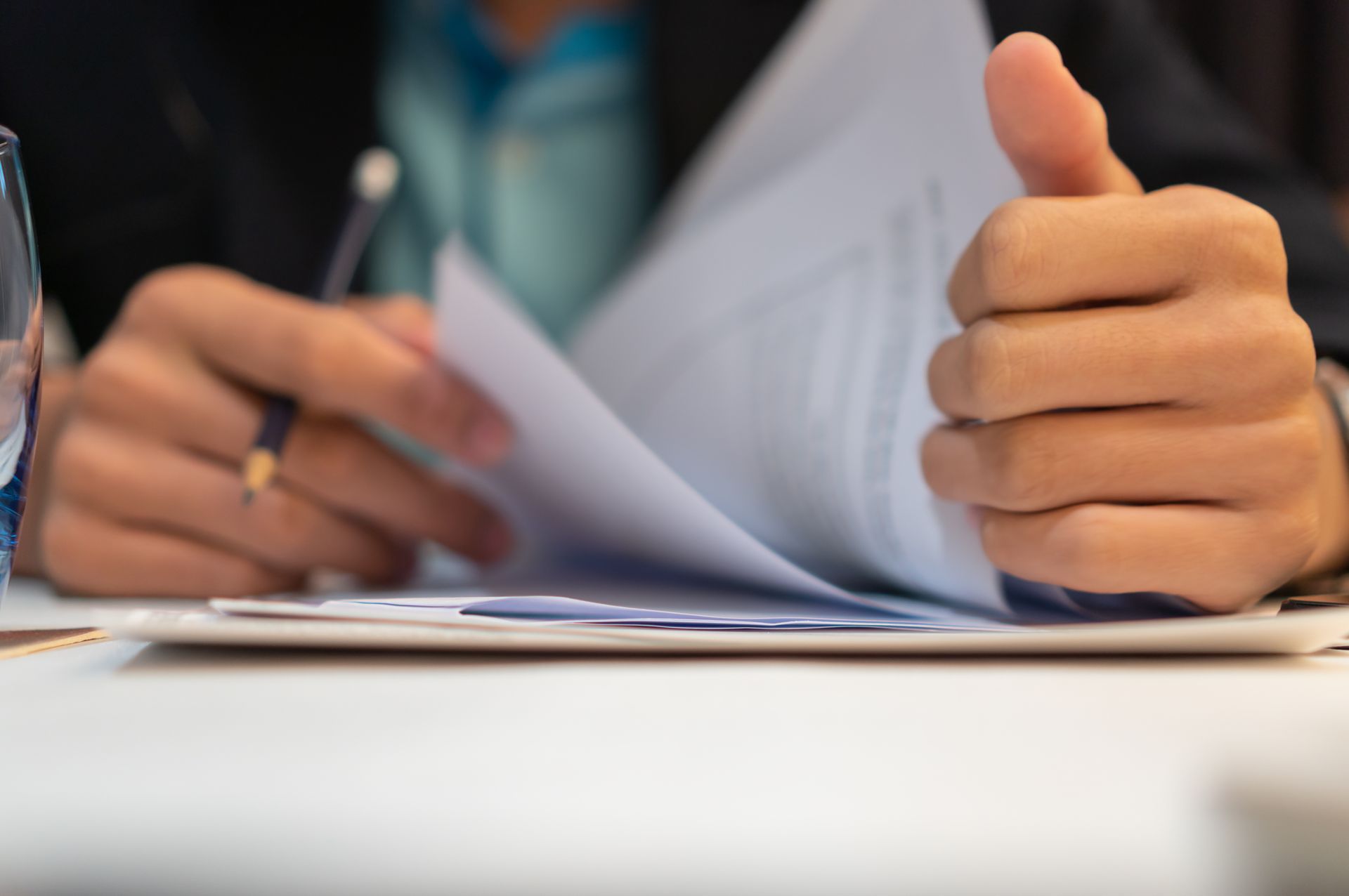 Person flipping through documents, holding a pen, and giving a thumbs-up.